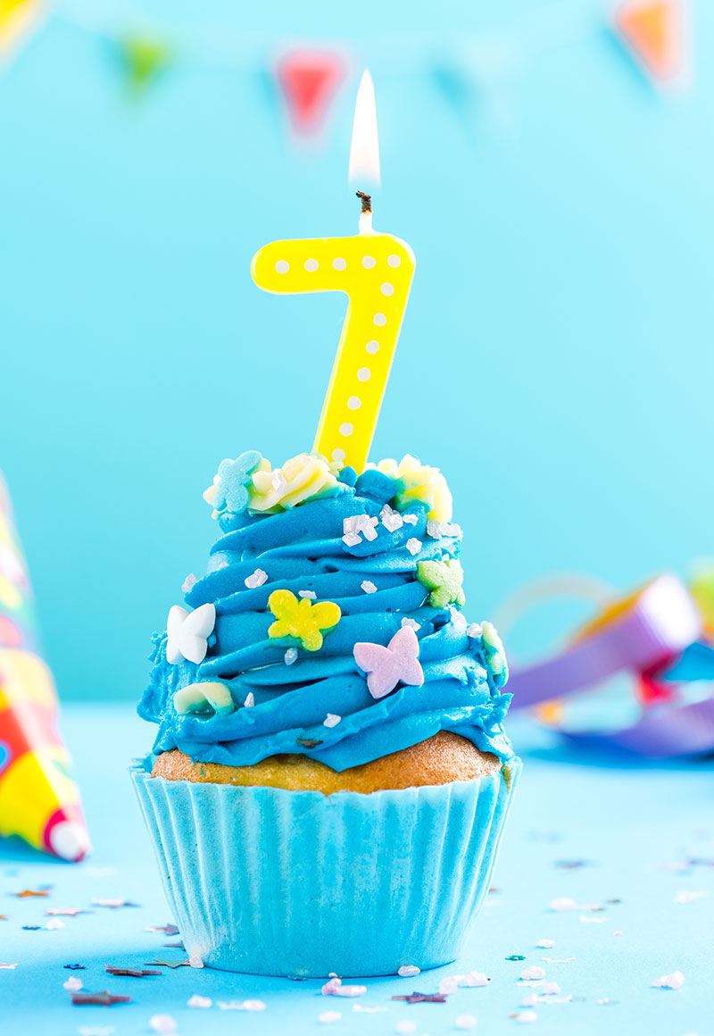a cupcake with a lit candle shaped like a 7 on it